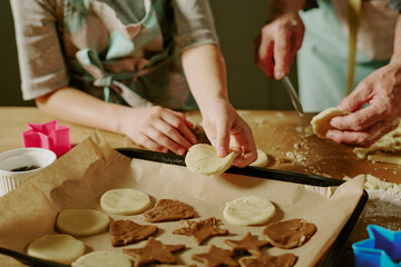 Culinary activity involving child and adult creating various cookie shapes from dough. Cookie cutters and dough on table creating fun and engaging baking experience