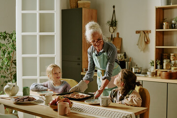 Elderly woman helping two young girls prepare breakfast in warm and inviting kitchen setting, with...