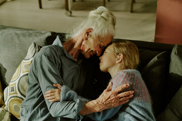 Elderly woman embracing young child while sitting on sofa in cozy living room. Warm interaction highlighting generational bond and affectionate relationship