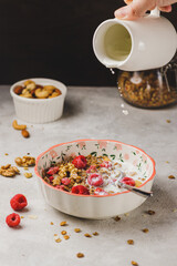 A plate with granola and raspberries, filled with milk