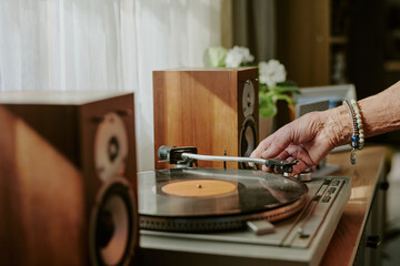Close-up of hand operating classic wooden turntable with spinning vinyl record in cozy room with natural lighting and white curtains