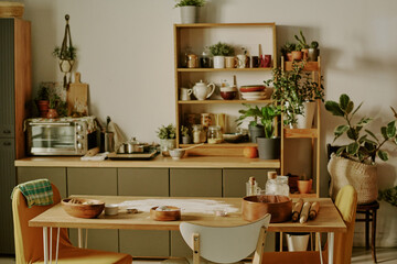 Modern kitchen with various plants and kitchenware displayed on shelves, and a wooden counter cluttered with baking ingredients and tools creating a cozy and inviting atmosphere