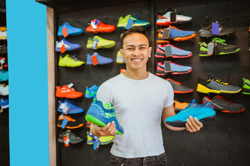 smiling asian salesman holding athletic shoes in front of display background