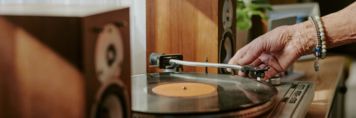 Close up of hand placing needle on vinyl record on turntable with speakers in background, detailed view highlighting turntables components and speakers