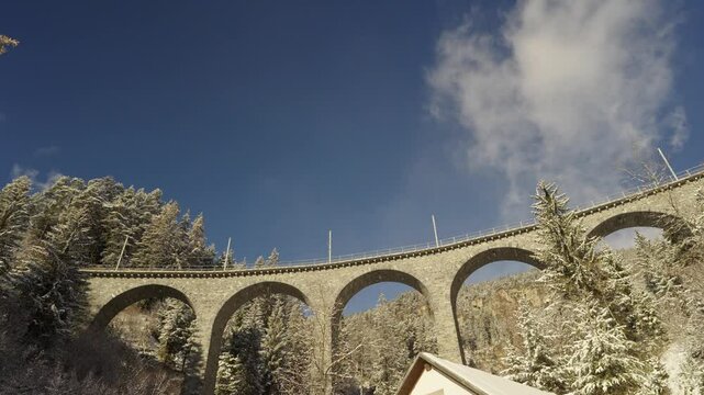 Train crossing famous Schmittentobel Viaduct of RHB narrow gauge railway at Swiss mountain village of Schmitten on a snowy autumn day. Movie shot November 22nd, 2024, Schmitten, Switzerland.