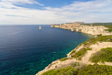 Scenic view of turquoise water and white cliffs with a sailing ship near Bonifacio, Corsica under a blue sky