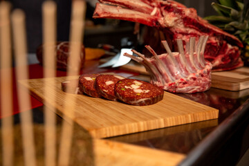 Slices of homemade sausage on a wooden cutiing board along with beef and lamb ribeyes. Butchers table with sausage and ribs.