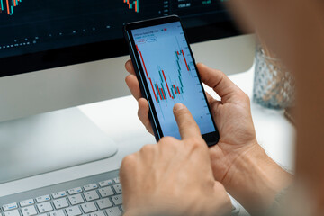 Smart stock investors pointing on screen with smartphone for market stock exchange along with laptop screen in highest dynamic investment rate, focusing data planning at modern workplace. Pecuniary.