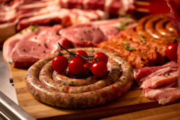 Sausages with tomatoes on them on a wooden table. Delicious meat table layout raw steaks and sausages. Premium organic meat to sell in market. Meat industry concept.