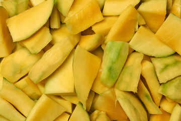pile of chopped ripe mango, vibrant yellow juicy fruit pieces to prepare mixed fruit salads or smoothies, food background taken from above