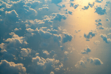 Clouds over a serene ocean reflecting the sunset glow, creating a tranquil view from above during late afternoon hours