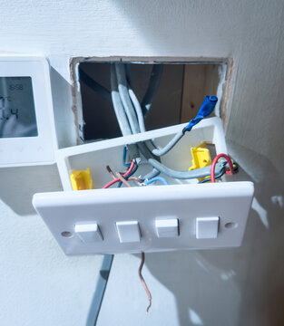 Close up of exposed electrical wiring in a wall socket, highlighting the risk of electrical hazards and DIY repair challenges home renovation or repair concept. electrical wires hanging from a wall.