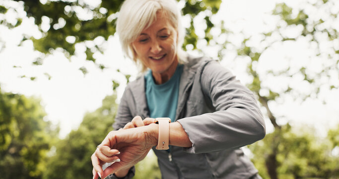 Fitness, check time and mature woman in park, smile and nature with training, wellness and exercise. Sports, person and runner with watch, outdoor and app to monitor heart rate, practice or challenge