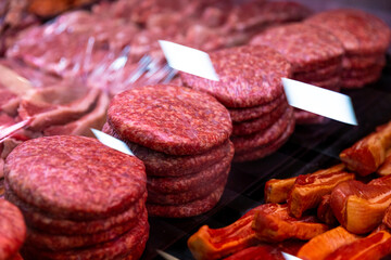 Burger cutlets on display in butchers shop vitrine made of beef meat. Row of beef burgers in a showcase in supermarket. Food industry concept.