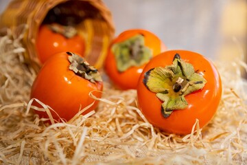 Close-Up of Ripe Persimmons in a Rustic Setting with Straw and a Basket