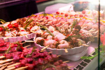 Raw chicken rolls seasoned with mixed peppers and rosemery on skewers. Diverse raw meat products for sale.