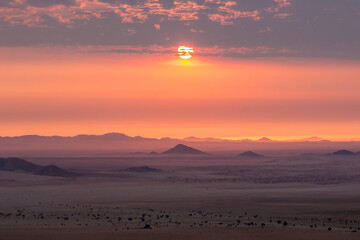 The setting sun breaking through the high stratus cumulus clouds over the vast open barren planes of the Sperrgebiet in Namibia