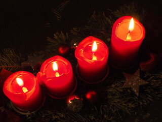 Vier rote Kerzen brennen nebeneinander auf einem Adventsgesteck, Blick von oben auf die Kerzen