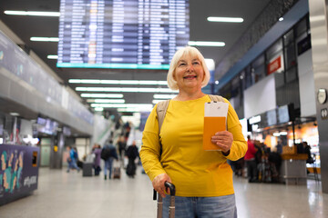 Traveler tourist happy smiling joyful fun mature elderly senior lady woman 55 years old with hand luggage, backpack holds passport and waits for flight travel at international airport terminal. 