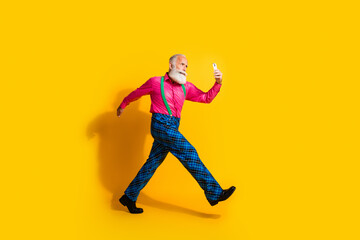 Full length photo of fashionable old gentleman walk hold device wear glamour garment suspenders isolated bright yellow color background