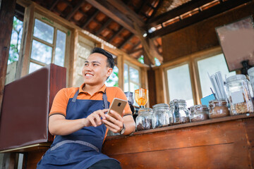 asian male coffee shop barista sitting and using phone for texting
