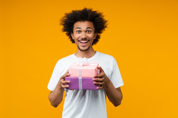 Studio shot of attractive happy smiling birthday boy guy posing with a of pile decorated gift boxes...