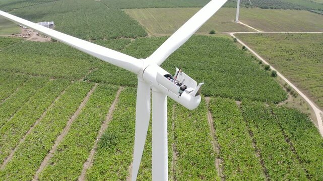 Drone ascending on a worker doing maintenance on a wind turbine in agricultural field