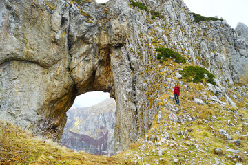 Šuplja vrata in Prokletije National Park: a woman in a red sweater stands near a natural arch in the rock. A female tourist visits one of the beautiful places in the Montenegrin mountains. © tanyatorgonskaya
