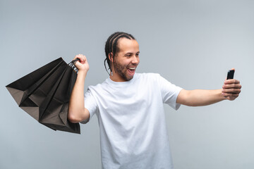 Studio shot of euphoric happy smiling man customer taking selfie with a bunch of shopping bags in...