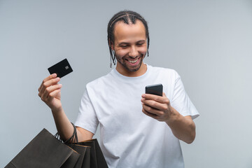 Studio portrait of happy smiling young African American man customer enjoying Black Fridat sale, doing shopping, ordering online via his smartphone, isolated over grey background