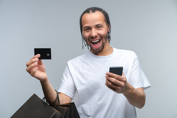 Euphoric young man customer posing over grey background with a bunch of shopping bags, credit card...