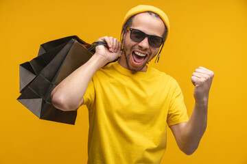 Studio shot of happy smiling attractive cheerful young man with a bunch of paper bags in hand...