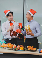 full length view of a group of business team wearing red Santa hat and exchange gift box together in the office for Christmas.