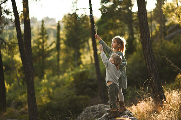 a boy and a girl are walking in the forest and blowing soap bubbles