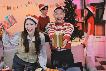 Group of happy Asian friends celebrating Christmas and decorate the Christmas tree indoors. Beauty woman with Christmas Gifts. New Year party. Woman hands decorate Christmas tree red ball, bauble.