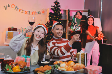 Group of happy Asian friends celebrating Christmas and decorate the Christmas tree indoors. Beauty woman with Christmas Gifts. New Year party. Woman hands decorate Christmas tree red ball, bauble.