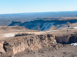 Expansive rocky cliffs and rugged terrain stretch across a vast plateau, with faint traces of snow...