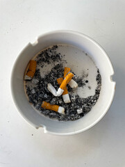 Cigarette in an ashtray, A pile of cigarette butts. The ashtray is white, full of cigarette butts and ash. Bad habits. Smoking is decreasing and has a bad effect on health.