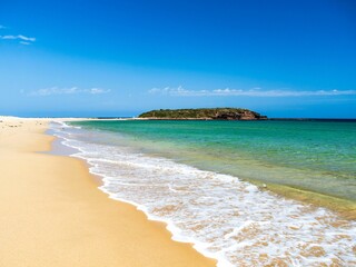 Pristine sandy beach with turquoise waters and a distant island under a clear blue sky