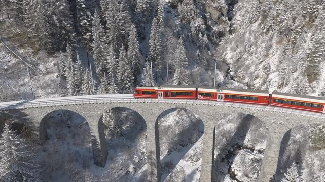Aerial view of train crossing famous Schmittentobel Viaduct of RHB narrow gauge railway at Swiss mountain village of Schmitten on an autumn day. Movie shot November 22nd, 2024, Schmitten, Switzerland.