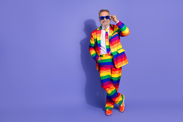 Charismatic elderly man in vibrant rainbow suit poses joyfully against a purple backdrop, embracing diversity and freedom