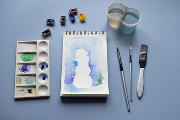 Watercolor painting of winter snowmen with paintbrashes, watercolor paints and palette