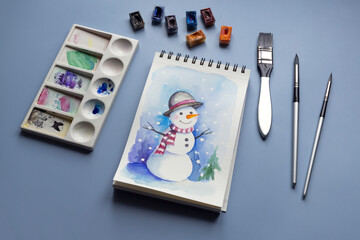 Watercolor painting of winter snowmen with paintbrashes, watercolor paints and palette