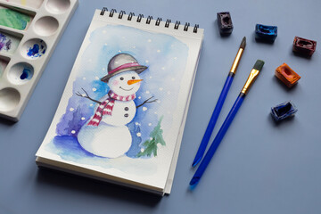 Watercolor painting of winter snowmen with paintbrashes, watercolor paints and palette