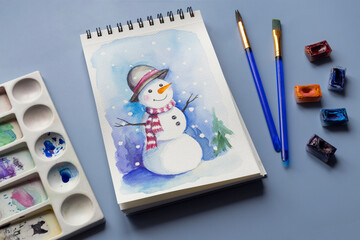 Watercolor painting of winter snowmen with paintbrashes, watercolor paints and palette
