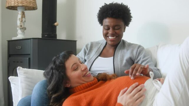 Affectionate pregnant partner and black woman cuddling and talking at home&nbsp;
