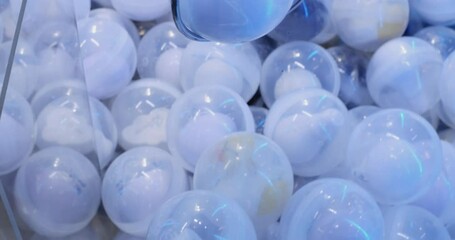 Metal claw crane descends, closing its grabber around a white surprise ball in an arcade game of skill, showcasing the excitement and challenge of winning a prize