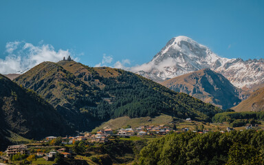 Gergeti Trinity Church perched on a hill with the snow-covered Mount Kazbek towering in the background, under a vibrant blue sky in Georgia