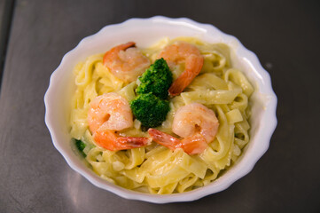 Creamy Fettuccine Alfredo with shrimp and broccoli on a white plate. Delicious italian pasta.