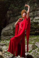 Asian girl in a beautiful red kimono and a Vietnamese triangular hat poses sexually in the bosom of nature in a rocky canyon